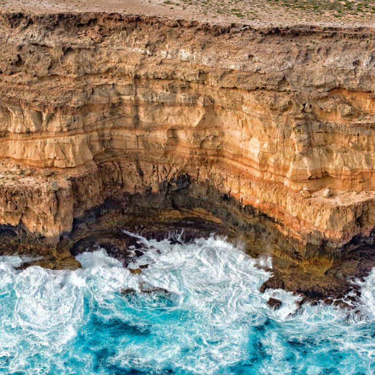 Dramatic coastal cliffs with turquoise waters crashing against them in Shark Bay